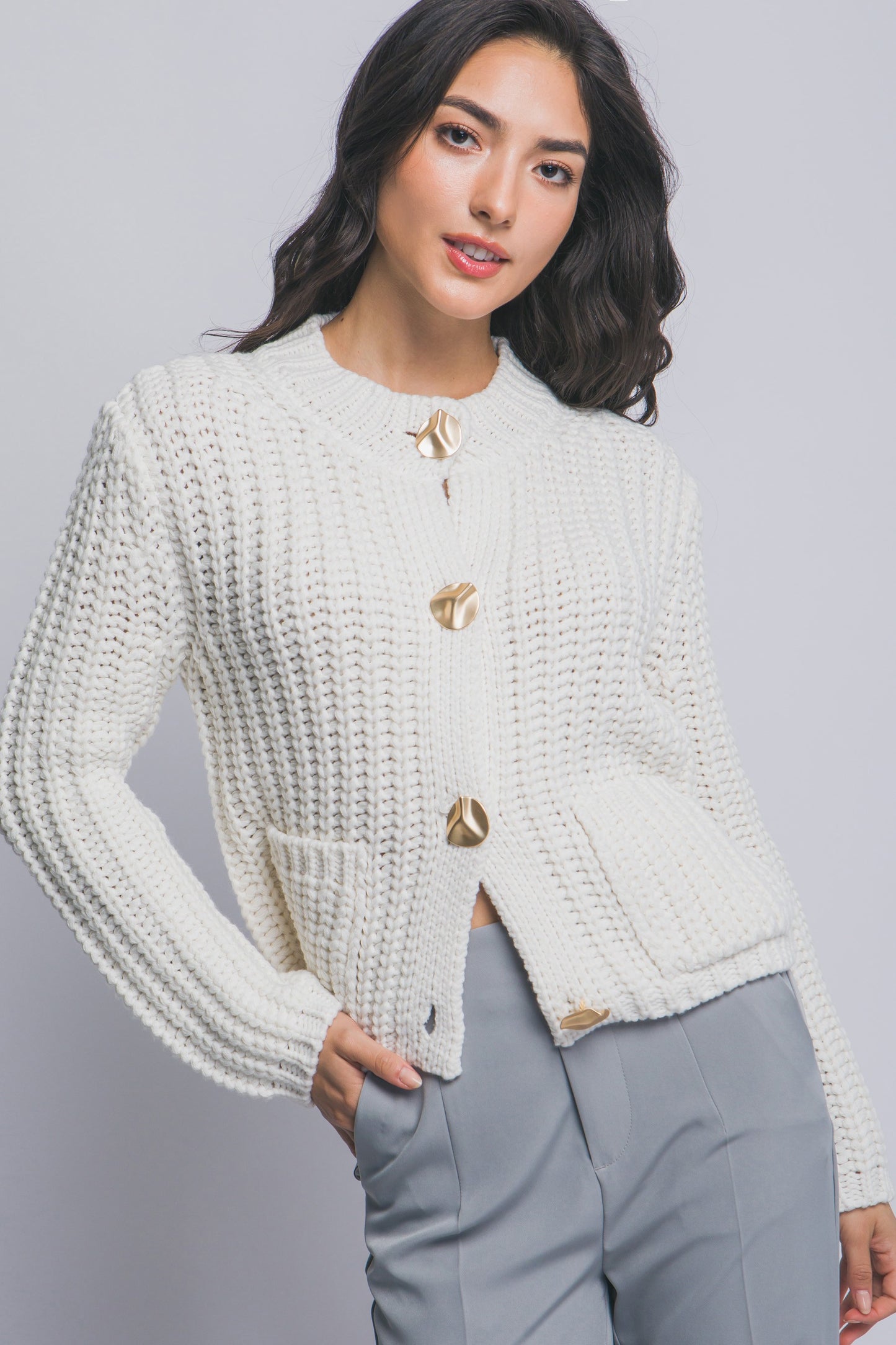 Woman wearing a white textured cardigan with gold buttons on a gray background