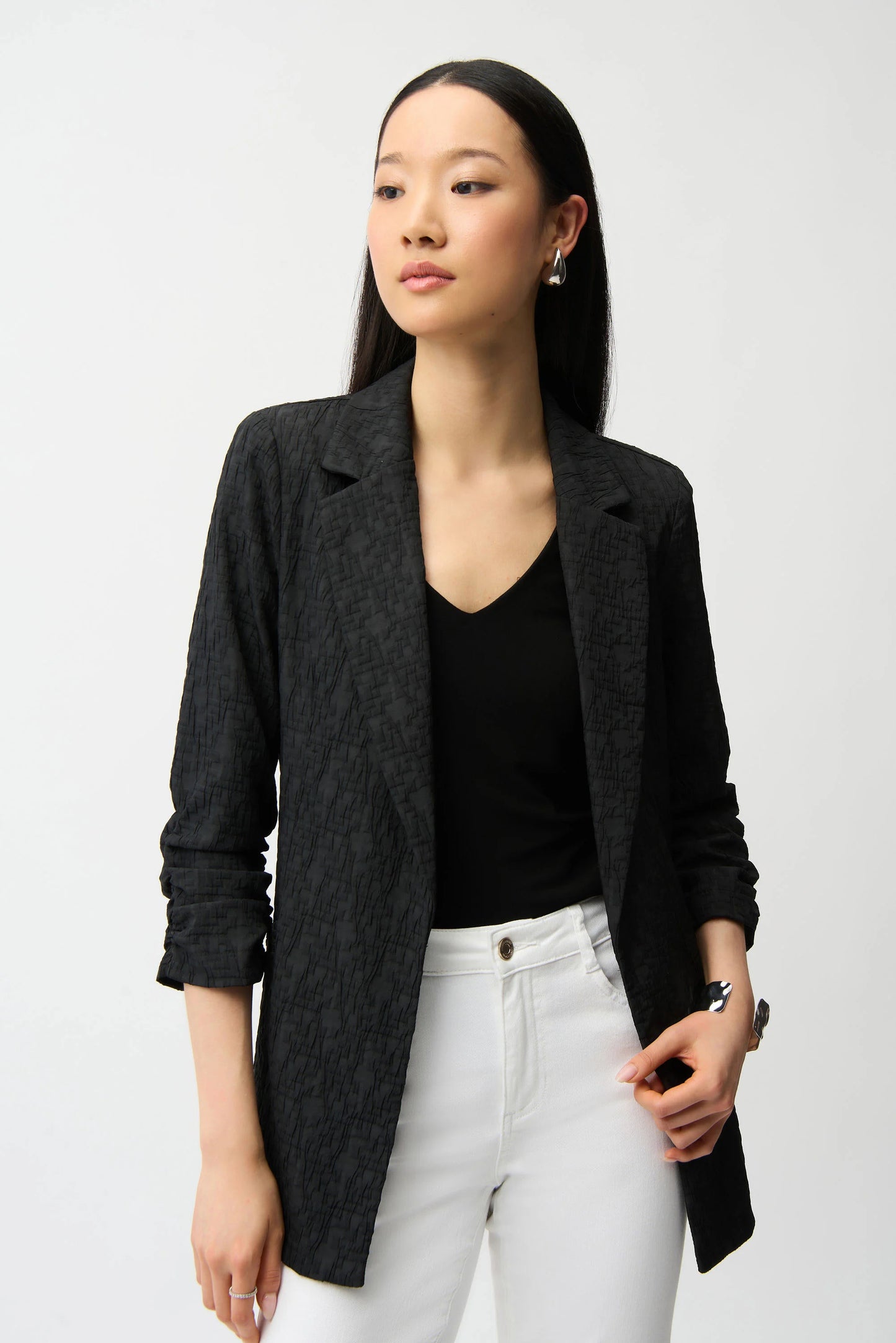 Woman wearing a black blazer, black top, and white pants on a light gray background