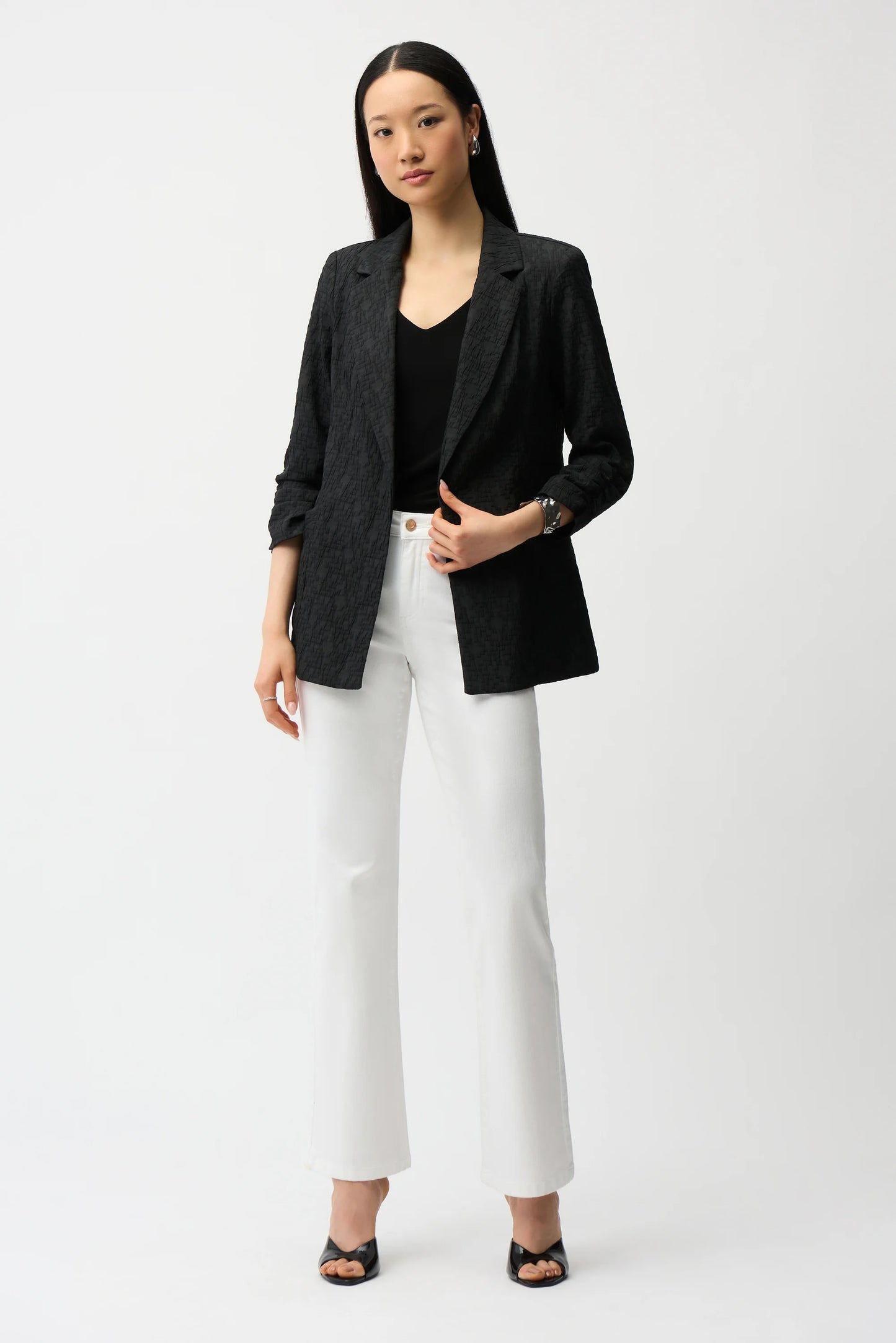 Woman wearing a black blazer, black top, and white pants on a white background