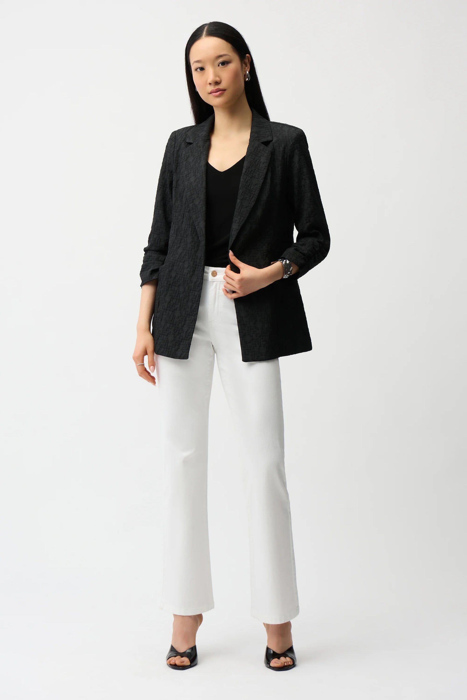 Woman wearing a black blazer, black top, and white pants on a white background
