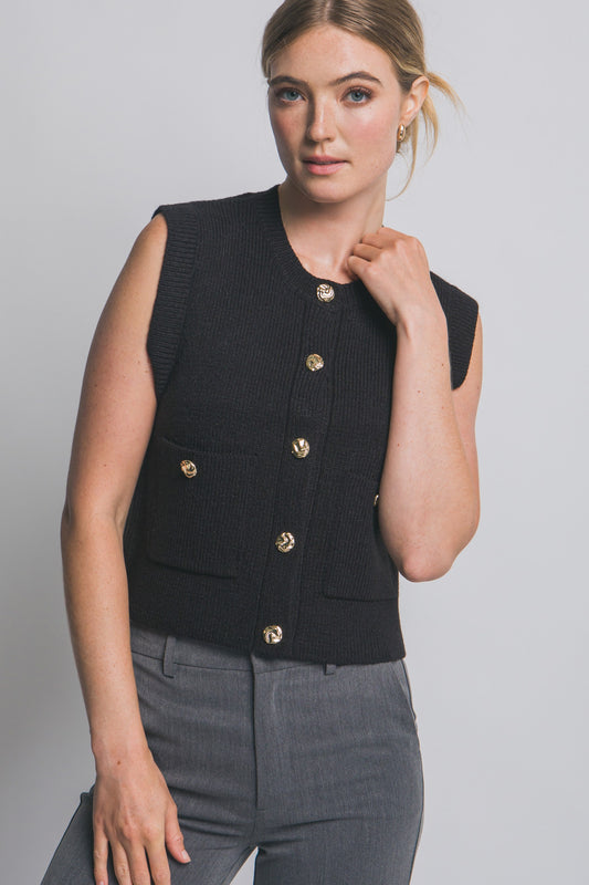 Woman wearing a black vest with gold buttons on a plain background