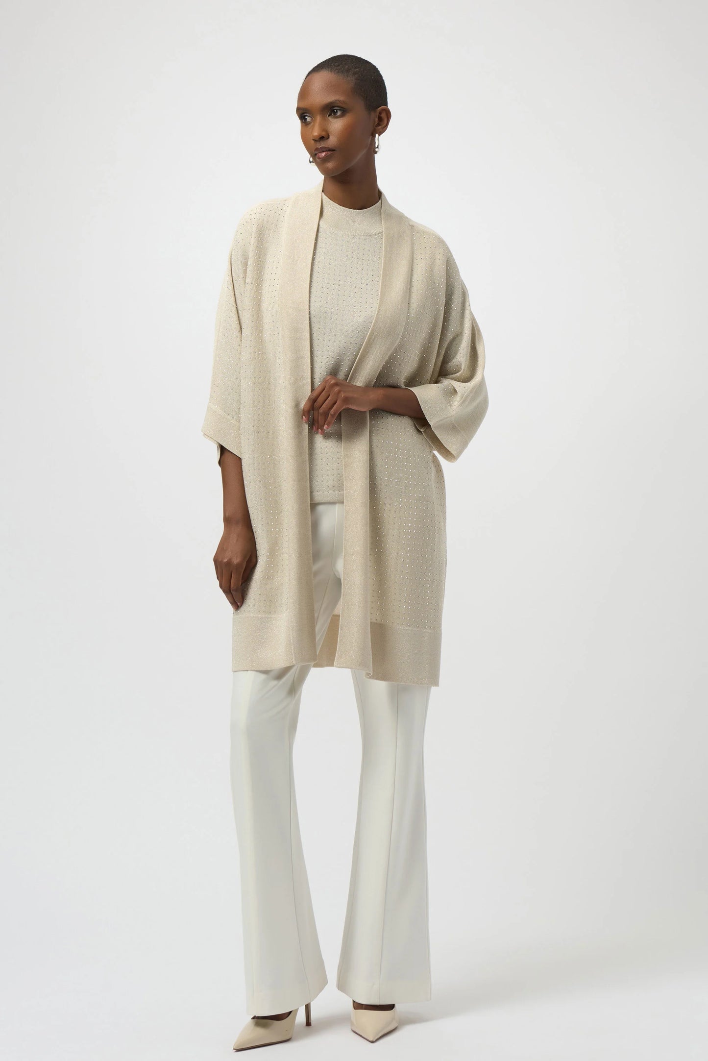 Woman wearing a beige cardigan over a white top and pants on a white background