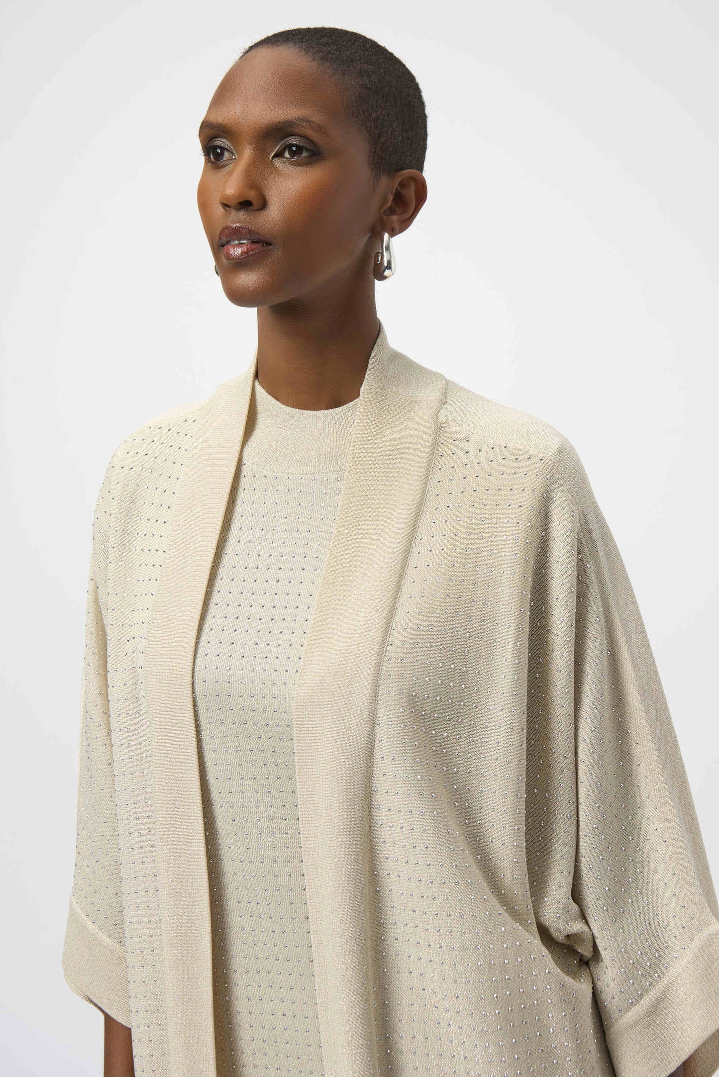 Woman wearing a beige textured cardigan over a white top on a plain background