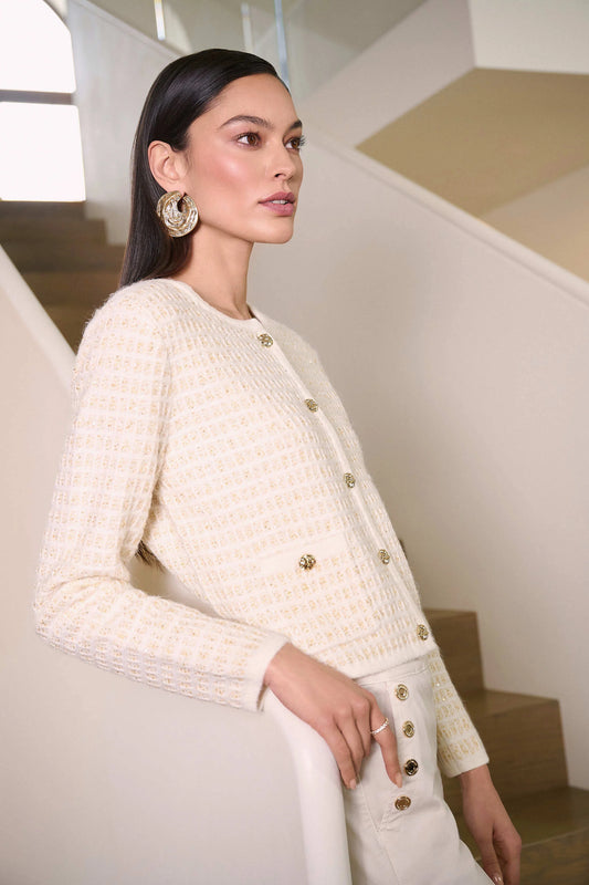 Woman wearing a cream-colored textured jacket with gold buttons in an indoor setting.