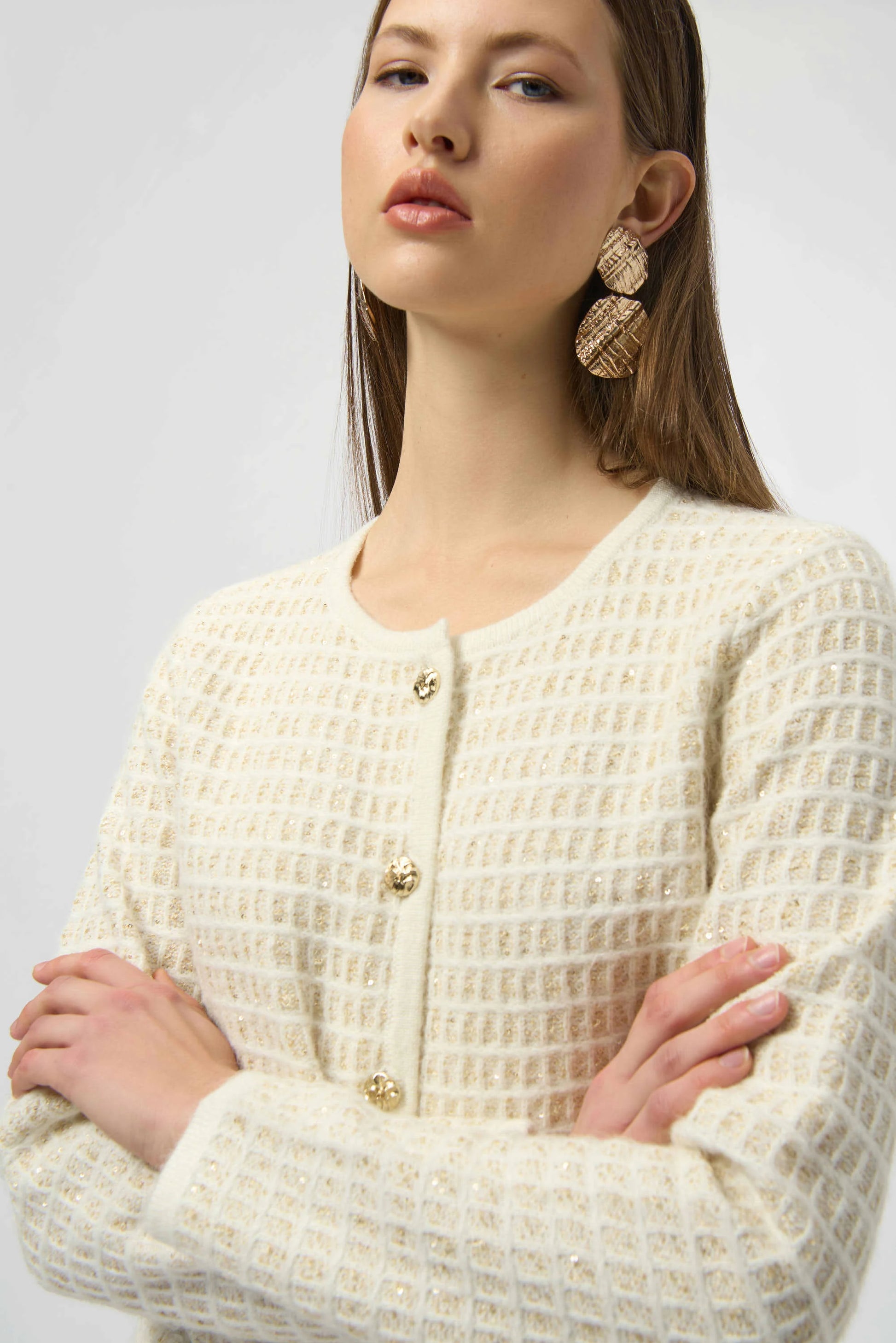 Woman wearing a cream-colored textured cardigan with gold buttons on a plain background