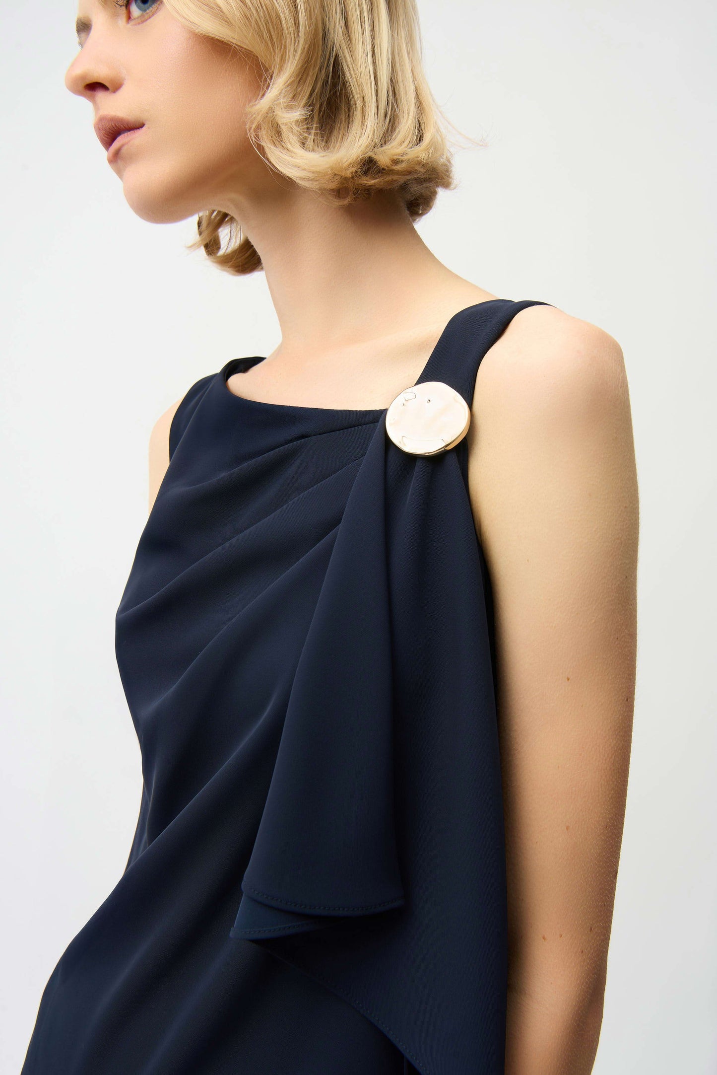 Woman wearing a navy blue dress with a large round brooch on a white background