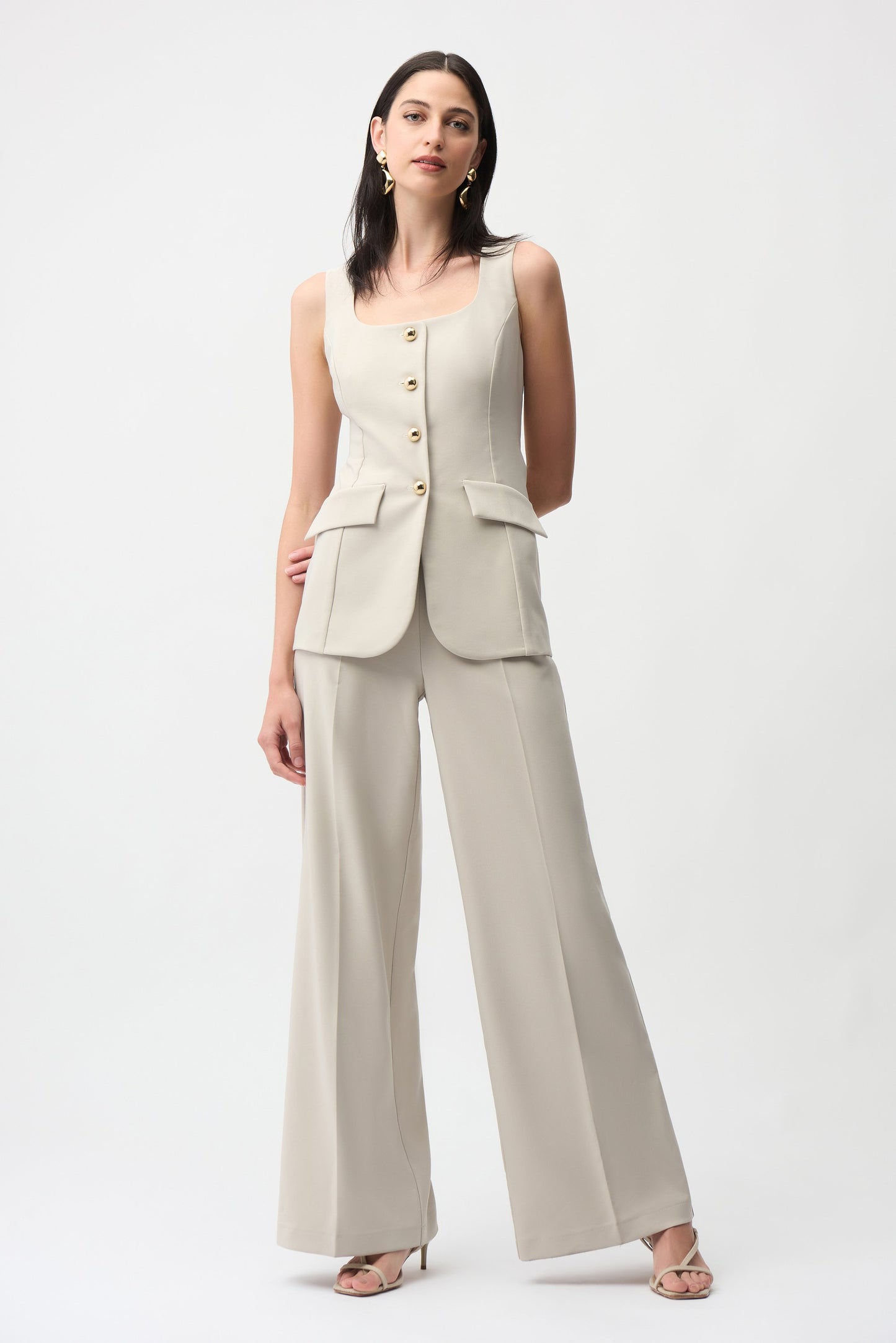 Woman wearing a beige sleeveless blazer and wide-leg pants on a white background