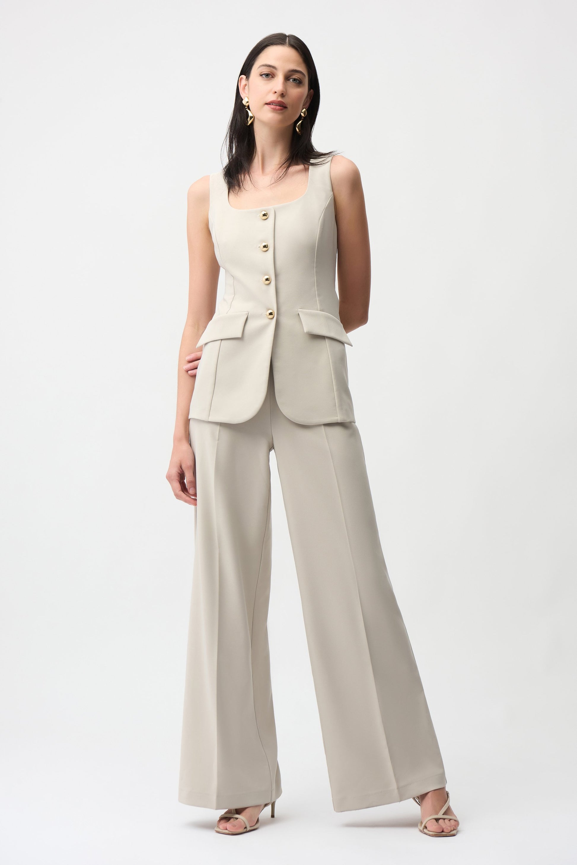 Woman wearing a beige sleeveless blazer and wide-leg pants on a white background