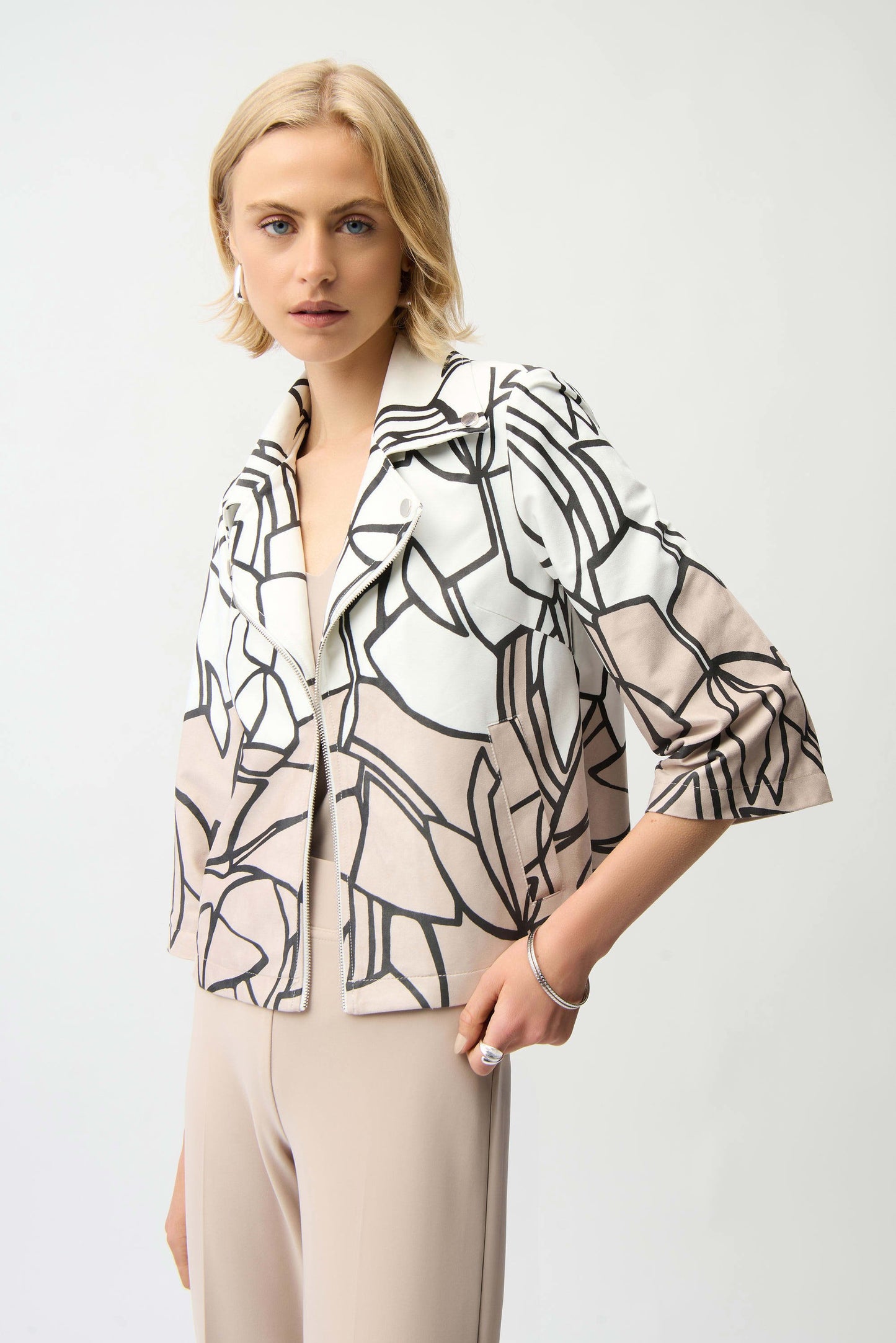 Woman wearing a stylish black and white patterned blouse with beige pants on a light gray background
