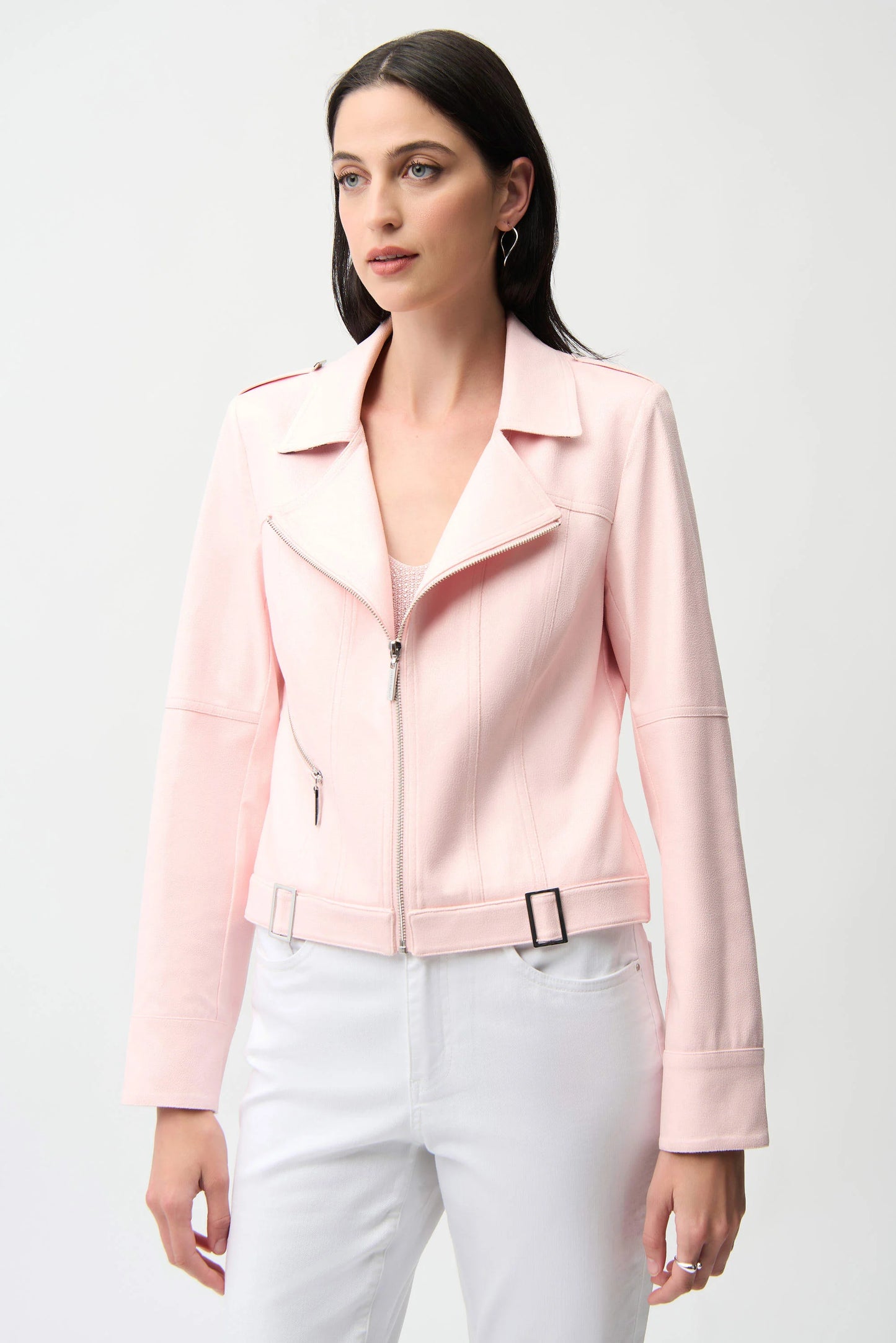 Woman wearing a light pink jacket and white pants on a plain background