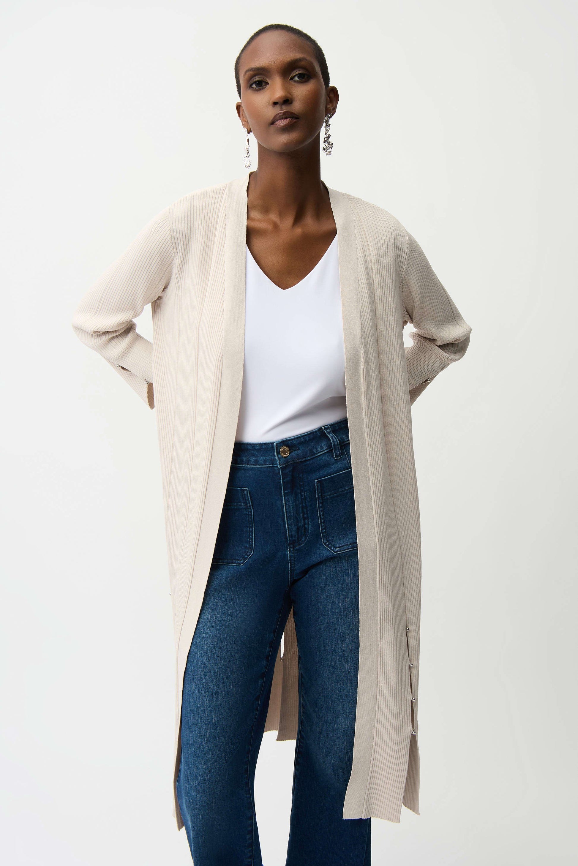 Woman wearing a beige cardigan, white top, and blue jeans on a white background