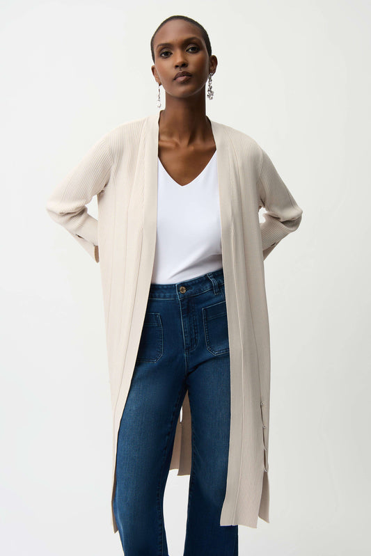 Woman wearing a beige cardigan, white top, and blue jeans on a white background