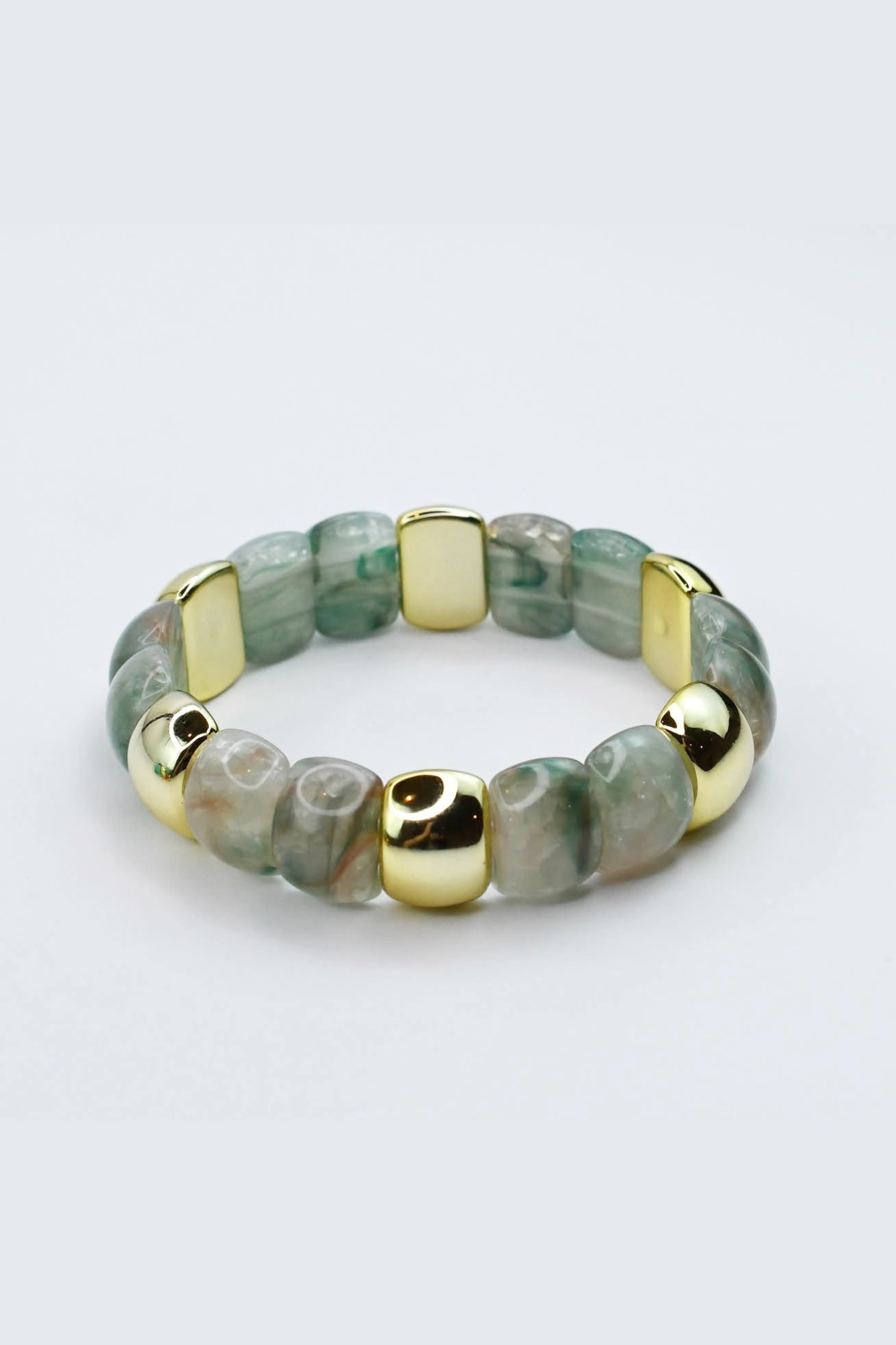 Bracelet with green beads and gold accents on a light gray background