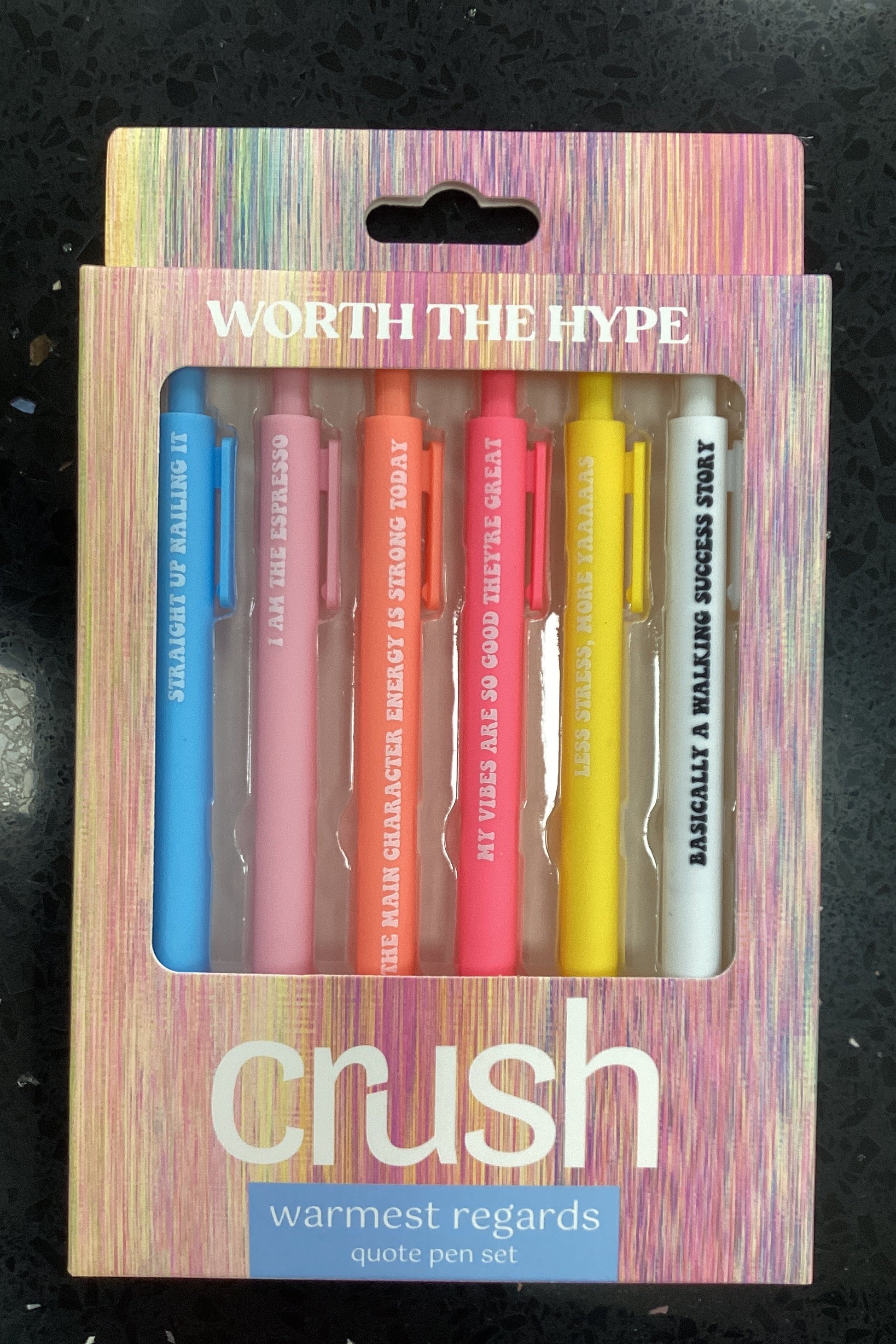 Set of colorful pens in a branded box on a dark surface