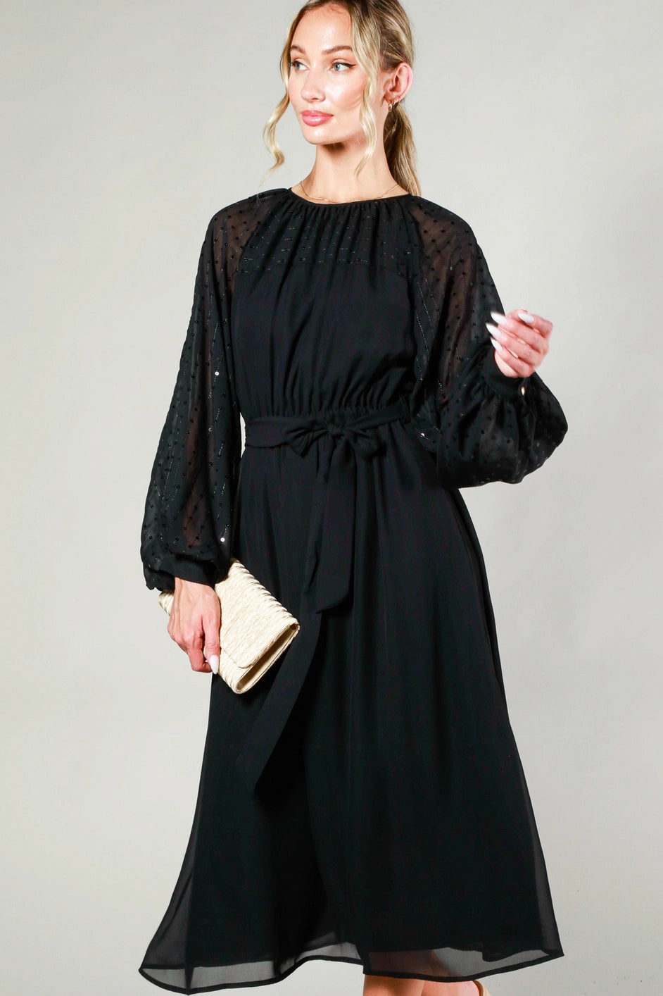 Woman wearing a black dress with sheer sleeves against a gray background