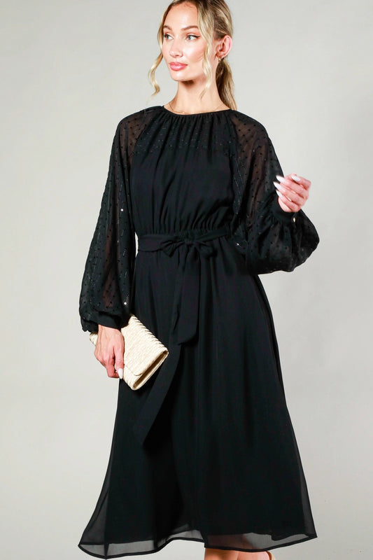 Woman wearing a black dress with sheer sleeves against a gray background