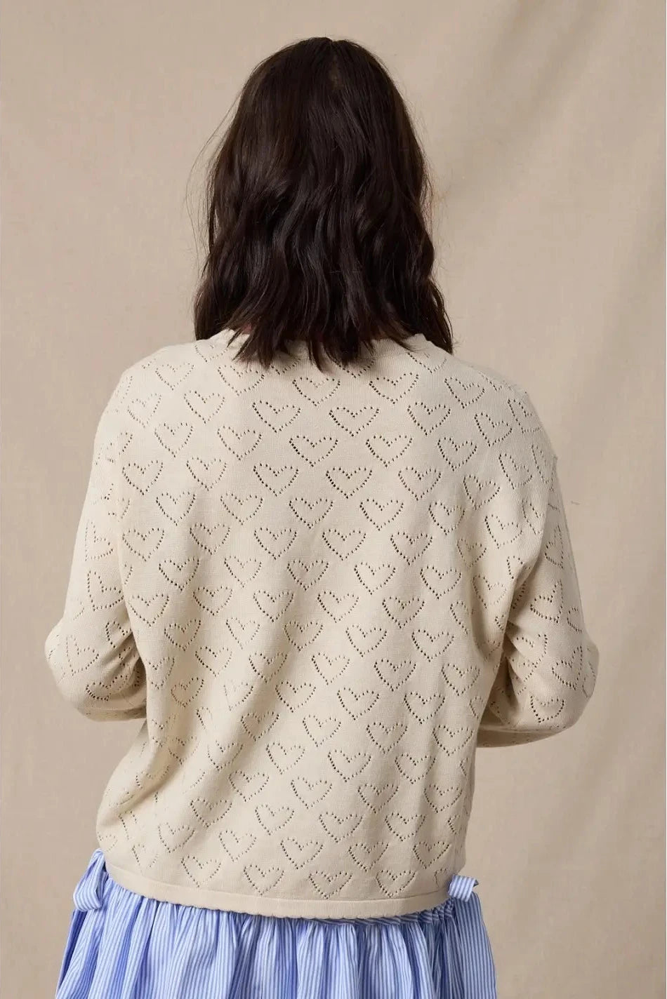 Person wearing a beige sweater with heart patterns against a beige background