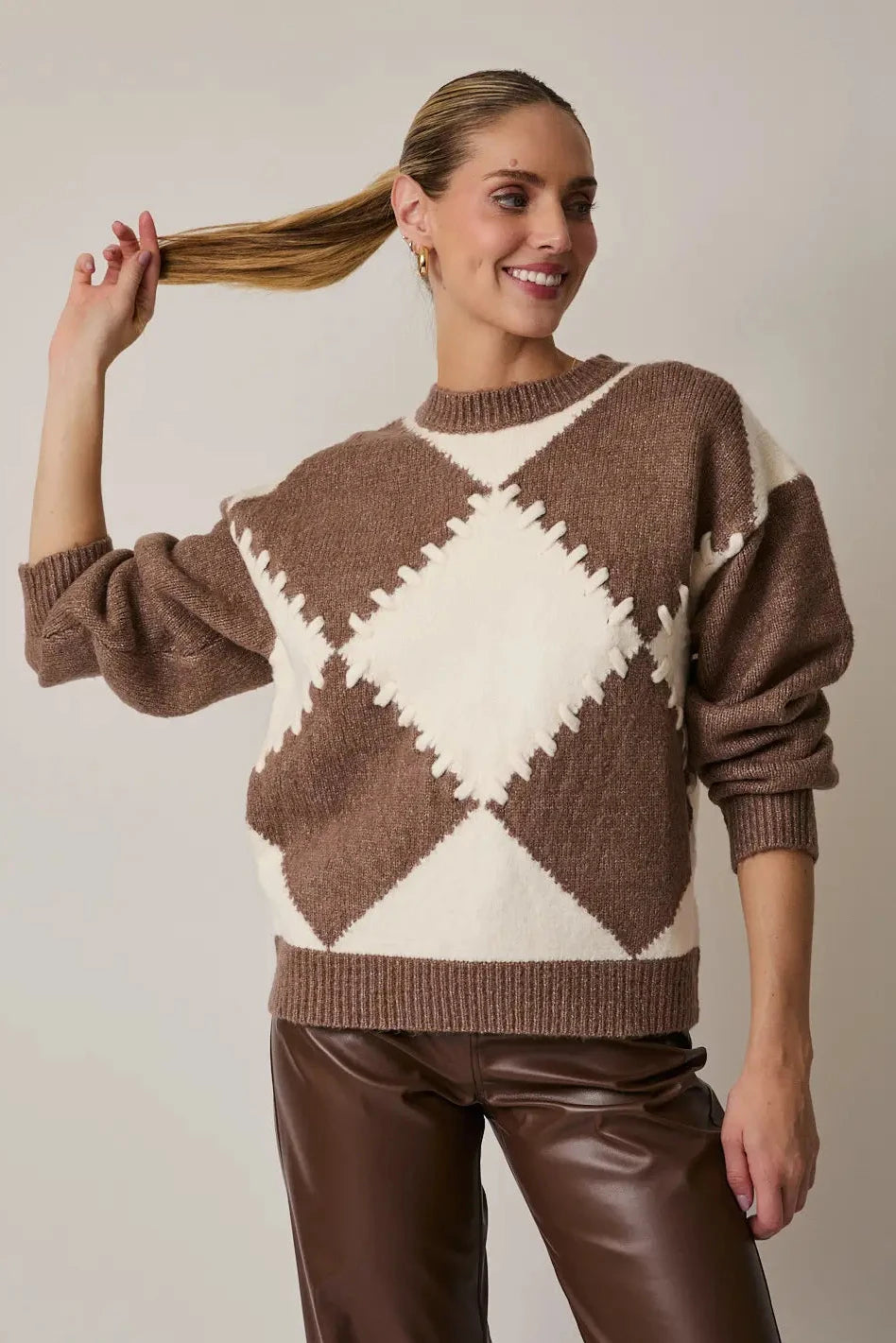 Woman wearing a brown and white argyle sweater against a plain background