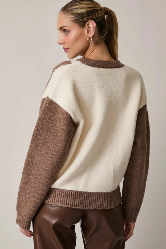Woman wearing a cream and brown sweater against a plain background