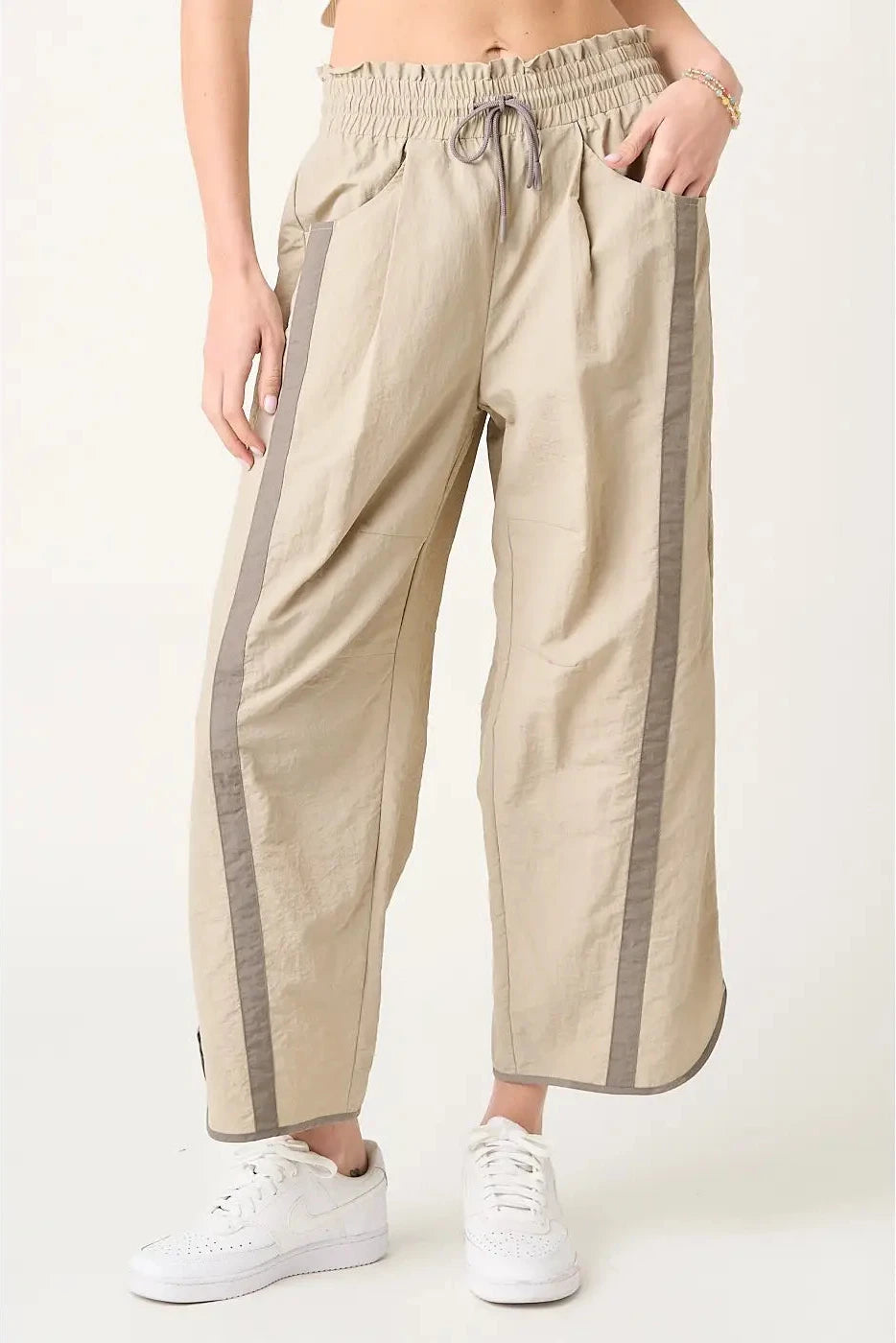 Beige pants with gray side stripes worn by a person on a white background