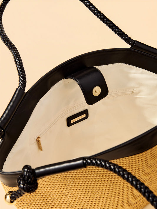 Close-up of a handbag with black handles and gold accents on a beige background