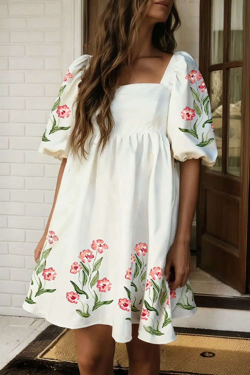 Woman wearing a white dress with floral embroidery standing indoors.