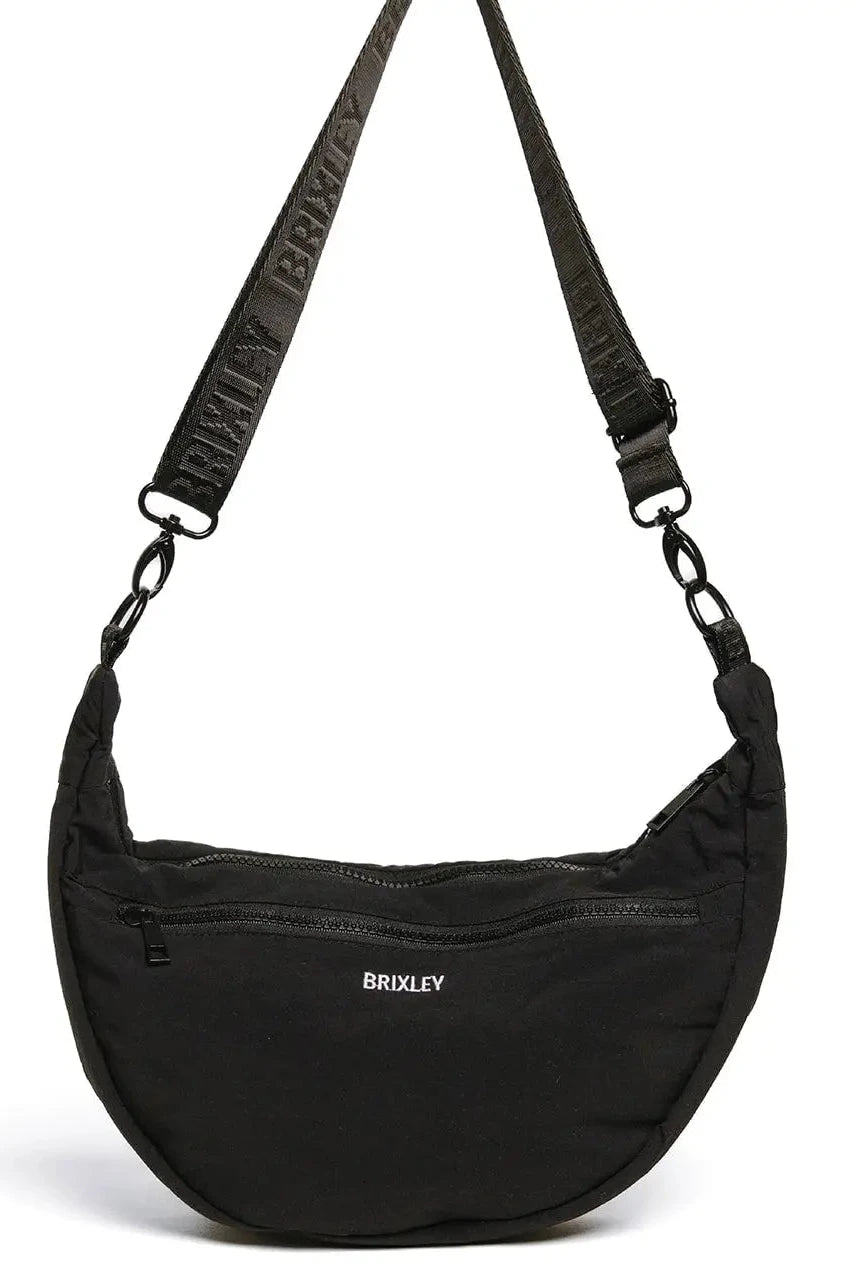 A black crescent-shaped nylon shoulder bag with a wide, adjustable black webbed strap featuring the brand name 'BRUXLEY' in white. The front of the bag has a zippered pocket with the 'BRUXLEY' logo printed in white, and the bag is photographed on a clean white background.