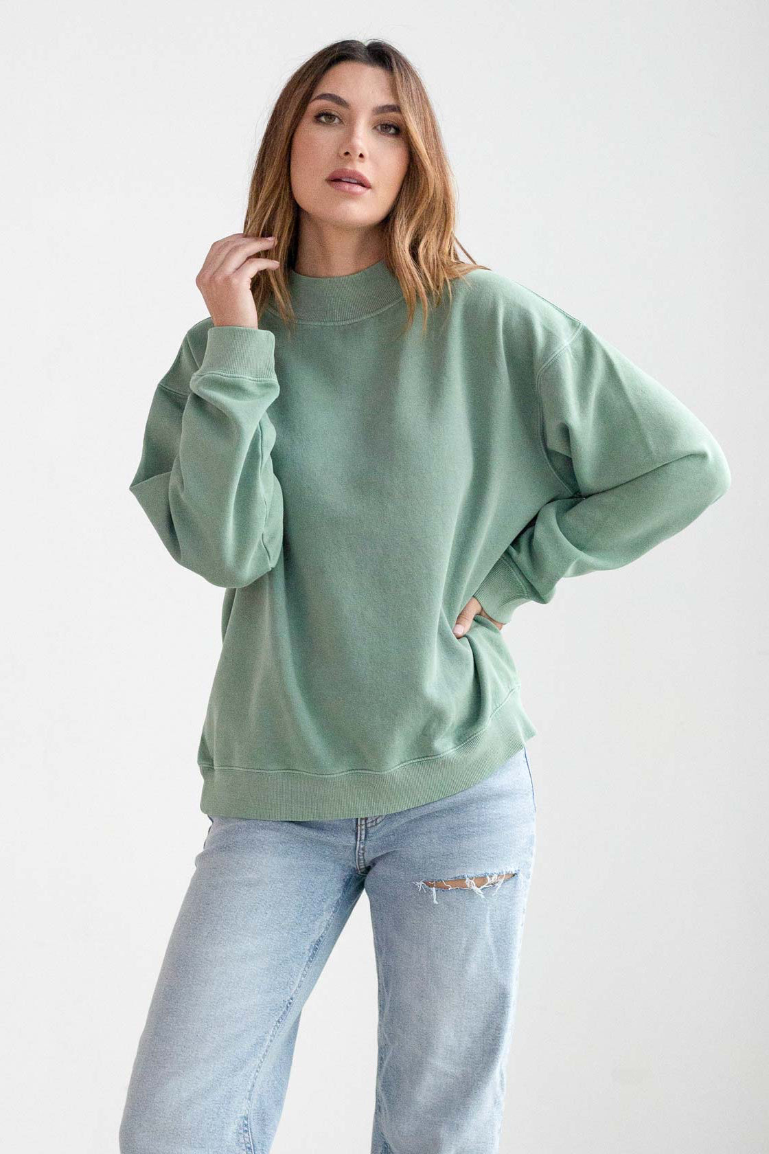 Woman wearing a green sweater and light blue jeans on a white background