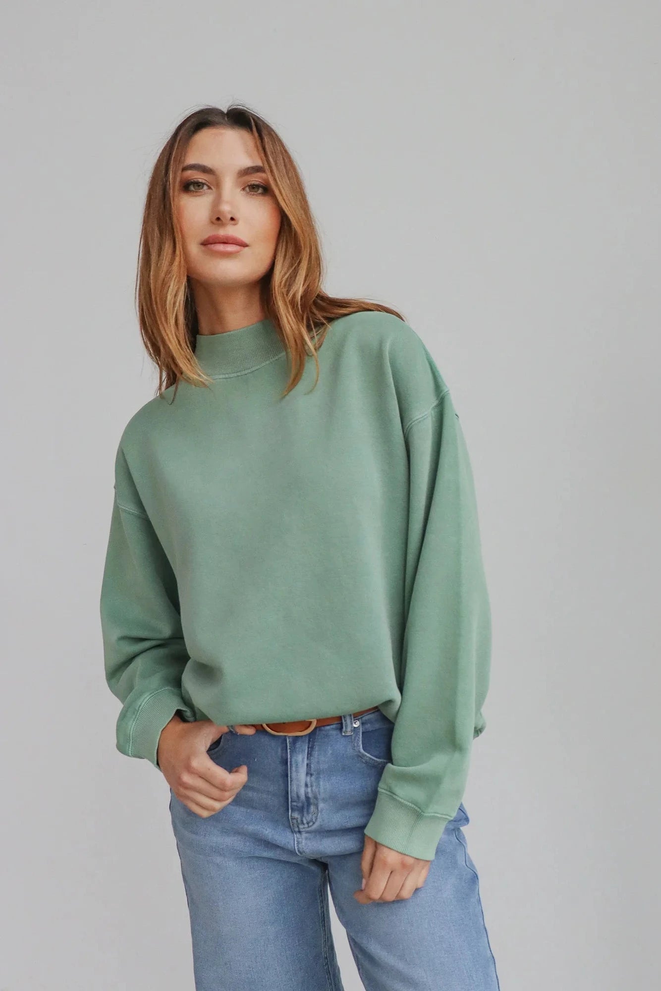 Woman wearing a green sweater and blue jeans against a gray background