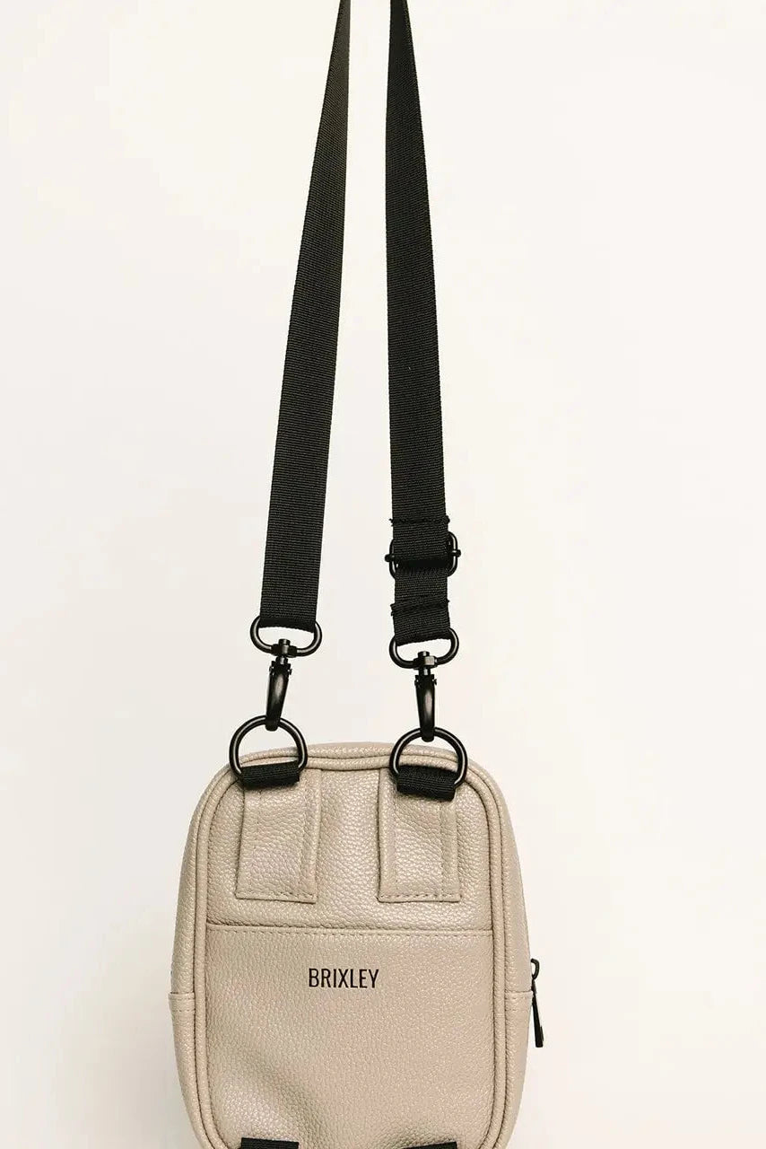 A small beige crossbody bag with a black adjustable shoulder strap and black hardware, featuring the brand name 'BRICKLEY' printed on the front, set against a plain white background.