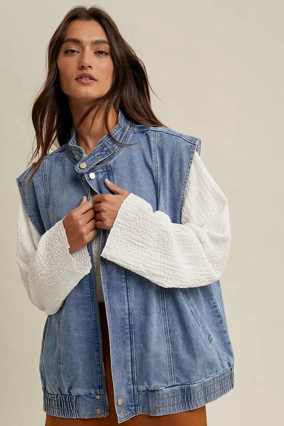 Woman wearing a denim jacket over a white sweater on a beige background
