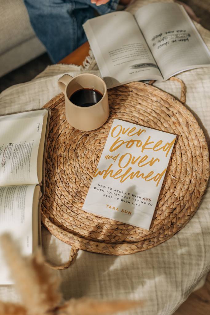 Open book, coffee cup, and 'Overlooked and Overwhelmed' book on a woven tray.
