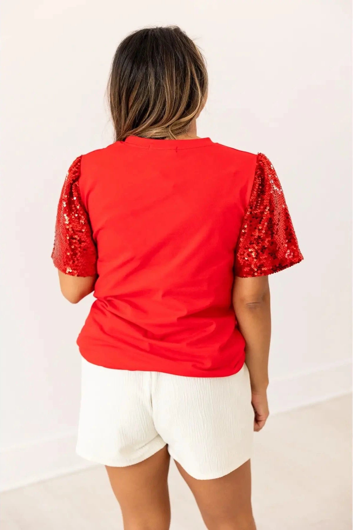Person wearing a red top with sequin sleeves on a white background