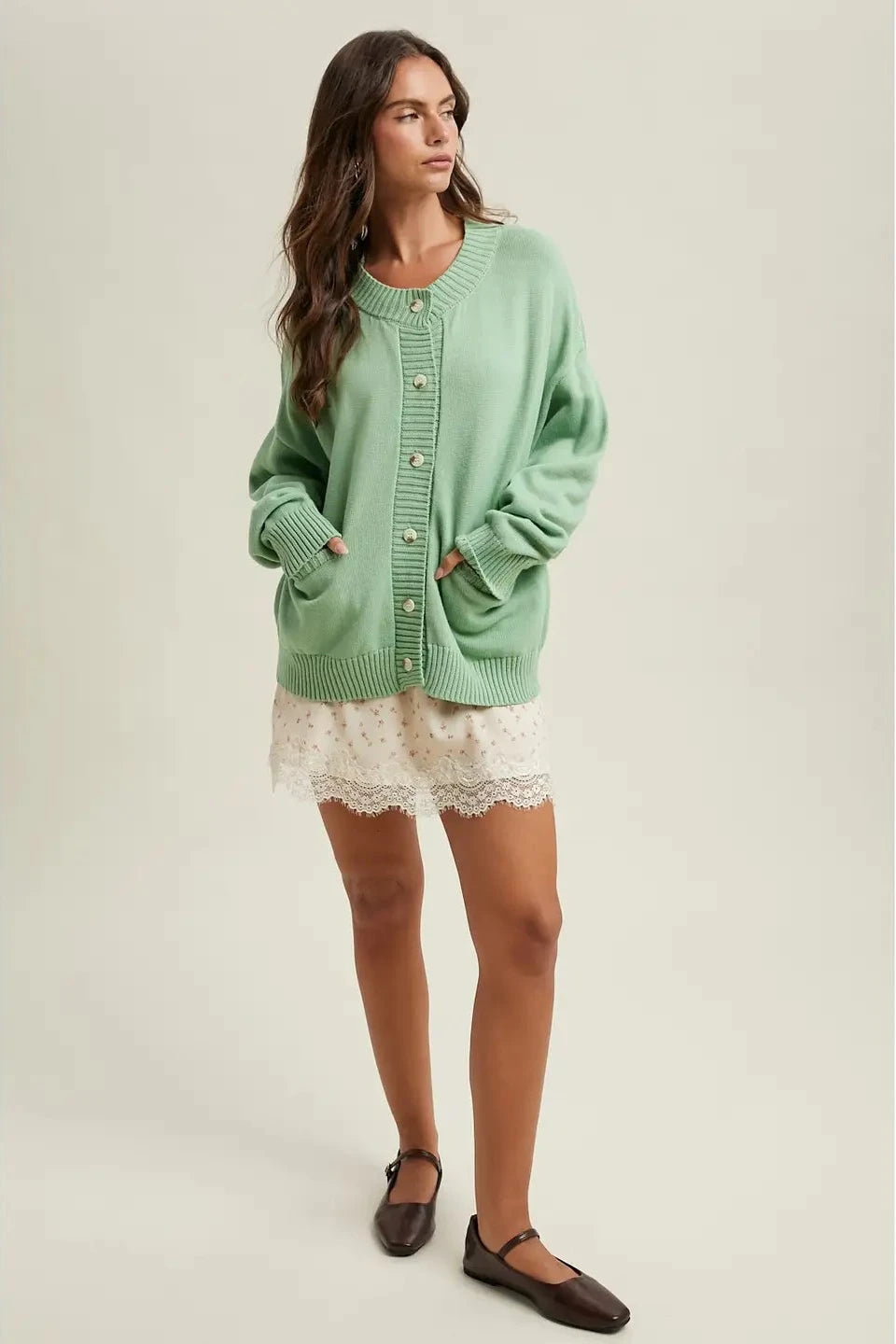 Woman wearing a green cardigan over a white lace dress on a beige background