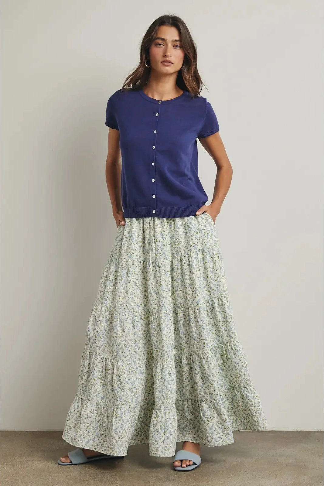 Woman wearing a blue top and long floral skirt on a plain background