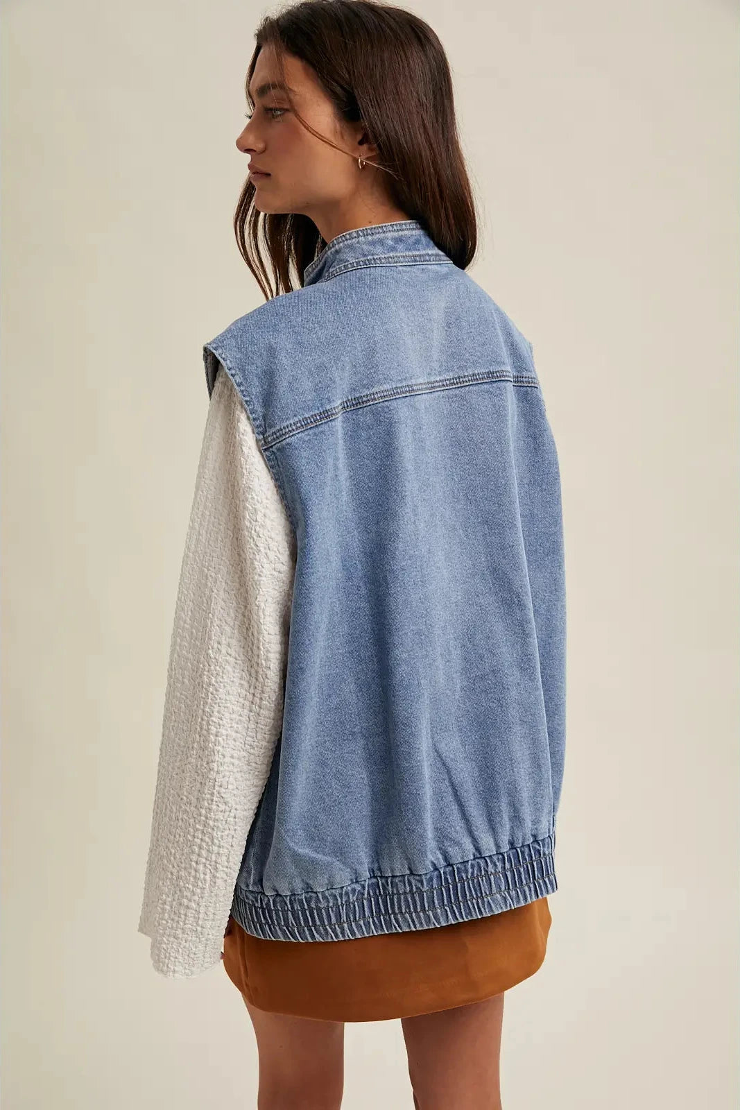 Woman wearing a denim vest over a white shirt with a beige background