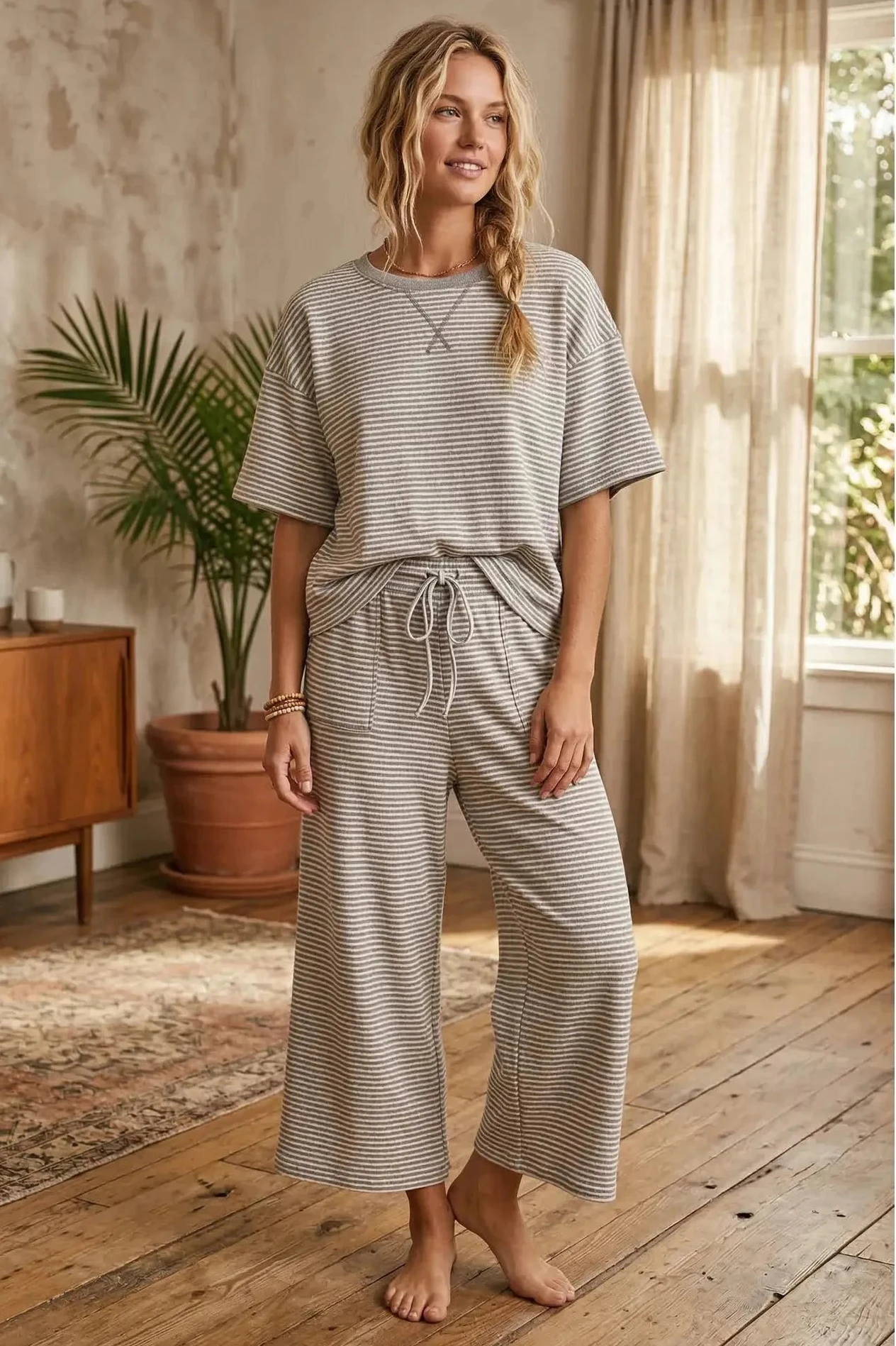 Woman wearing a striped outfit in a home setting with a plant and wooden floor.