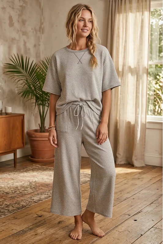 Woman wearing a striped outfit in a home setting with a plant and wooden floor.