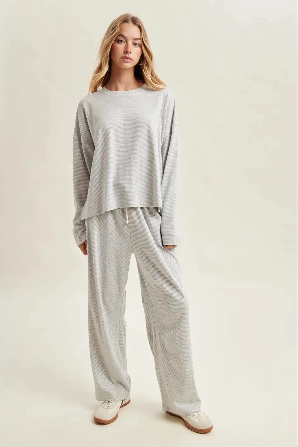 Woman wearing a light gray loungewear set on a plain background
