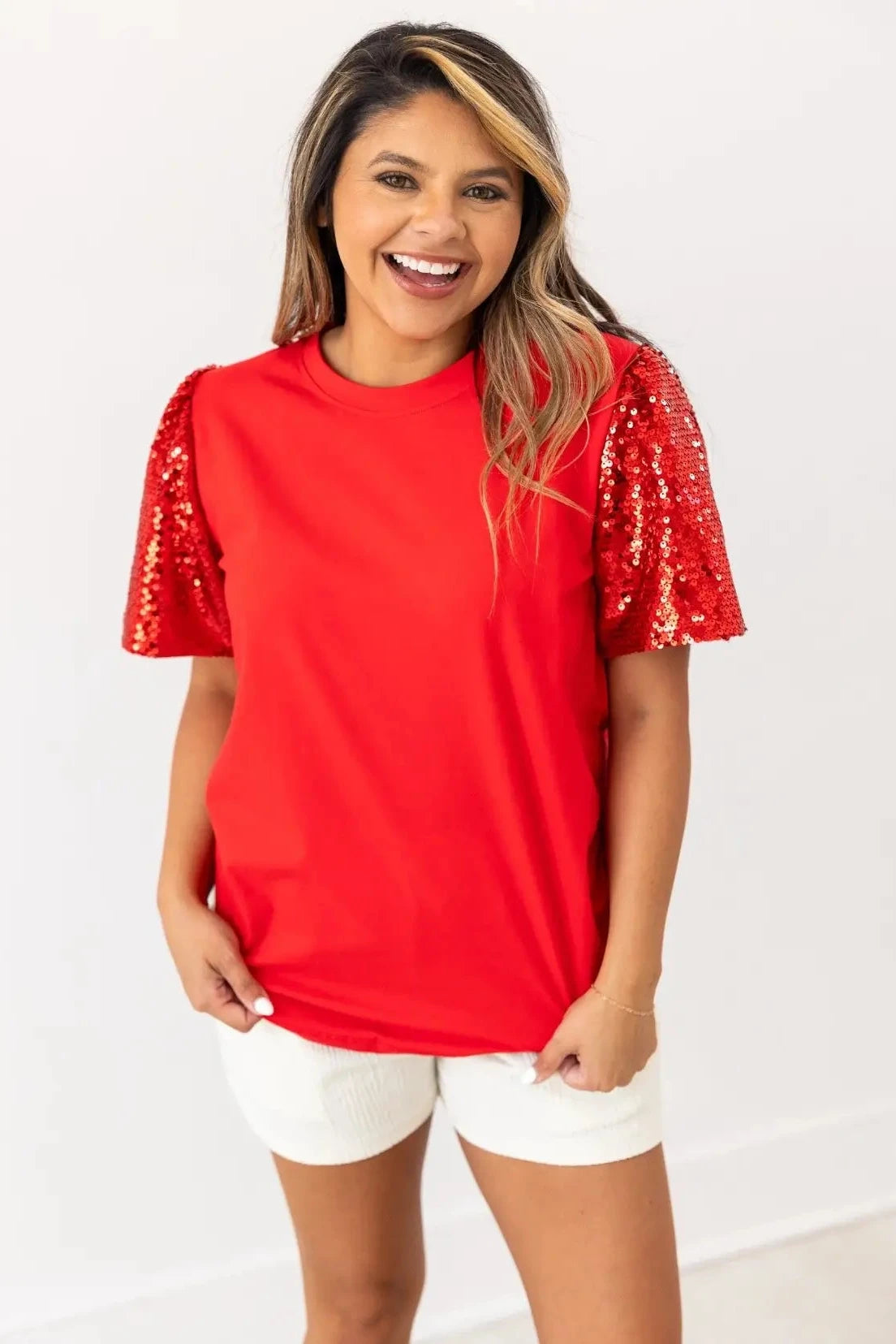Woman wearing a red top with sequin sleeves on a white background