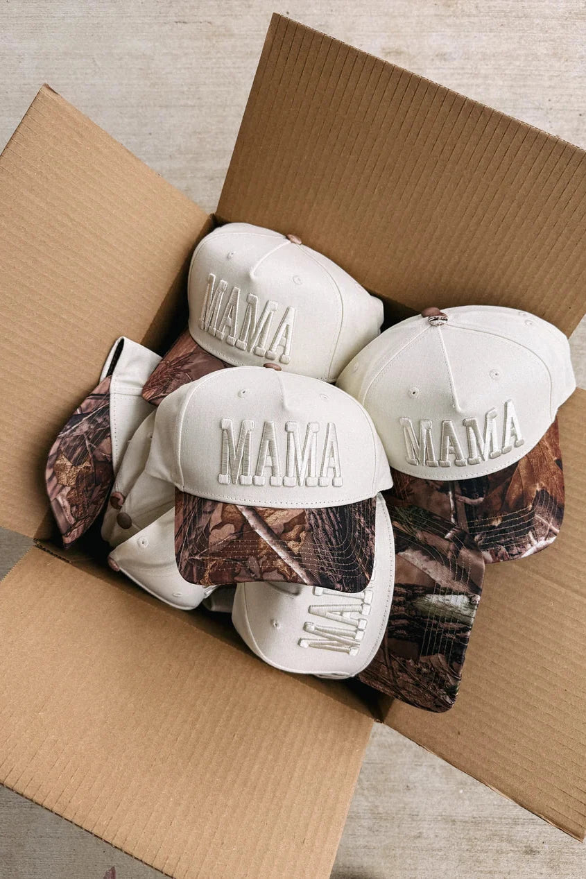 Box containing multiple 'MAMA' caps with camouflage patterns on a neutral background