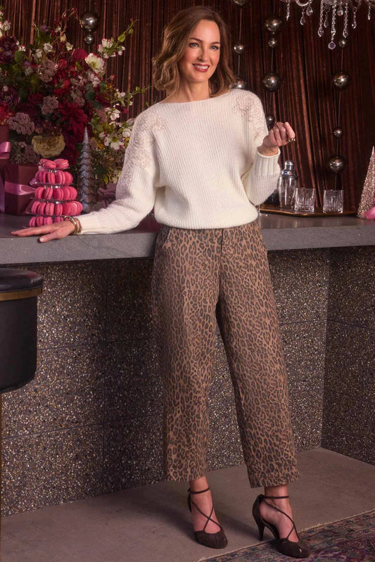 Woman in a white sweater and leopard print pants standing in a decorative setting with flowers and ribbons.