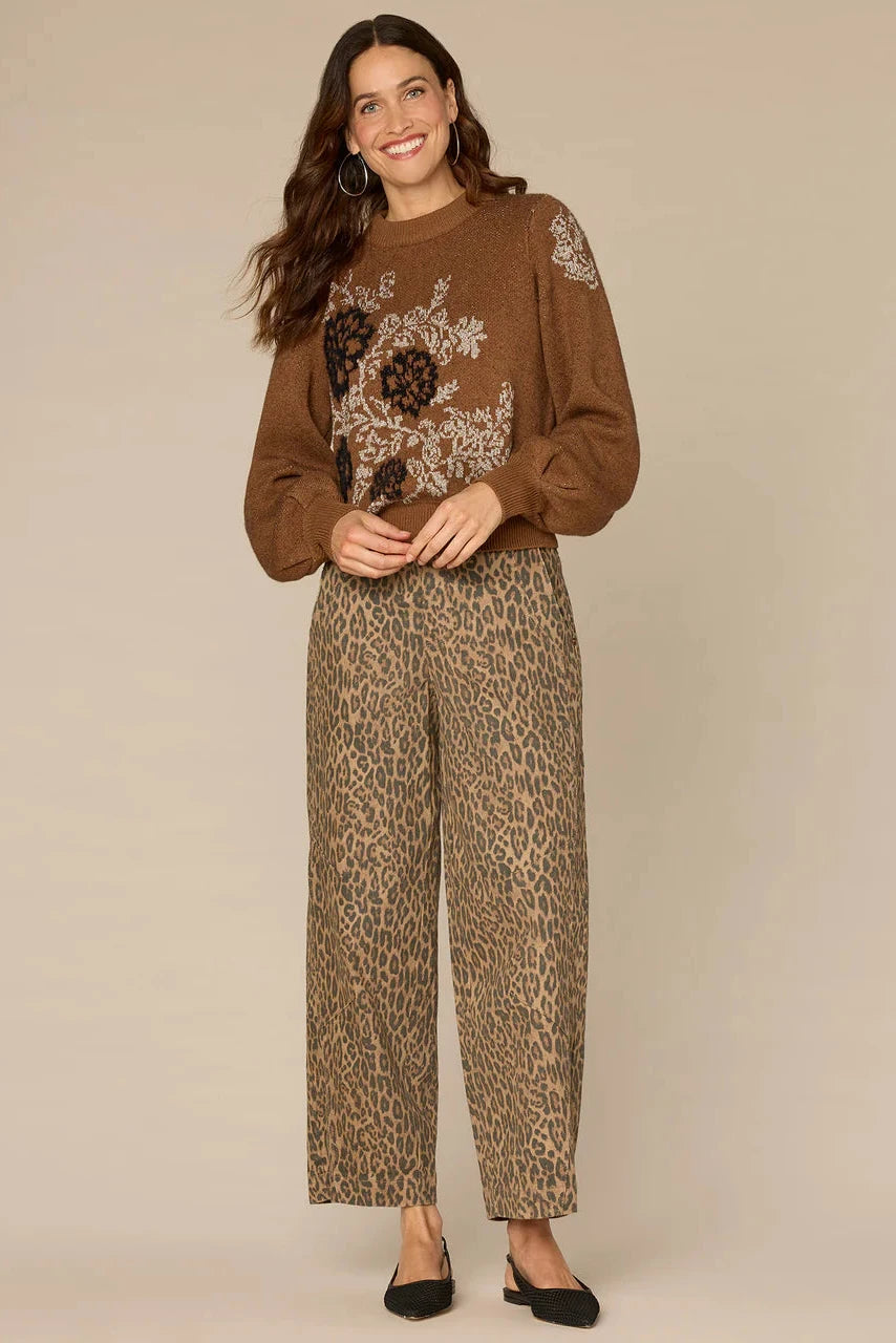 Woman wearing a brown sweater with floral embroidery and leopard print pants on a beige background