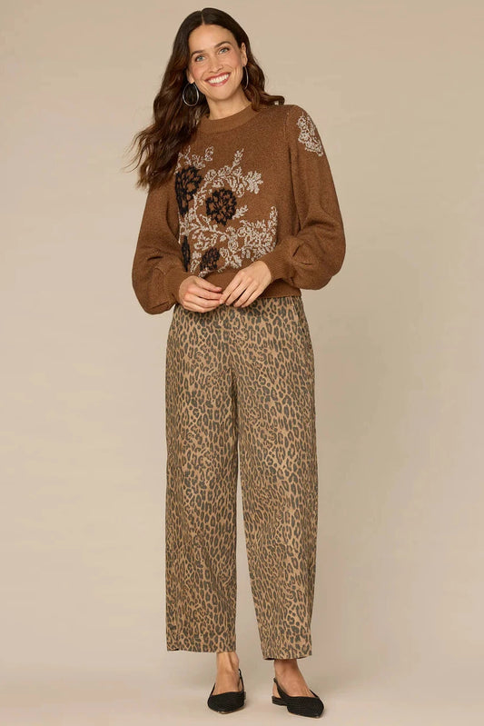 Woman wearing a brown sweater with floral embroidery and leopard print pants on a beige background