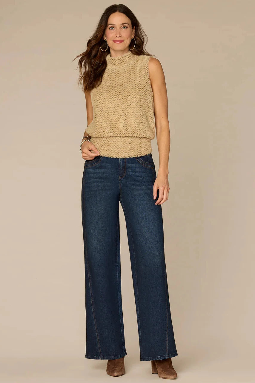 Woman wearing a beige sleeveless top and blue jeans on a beige background