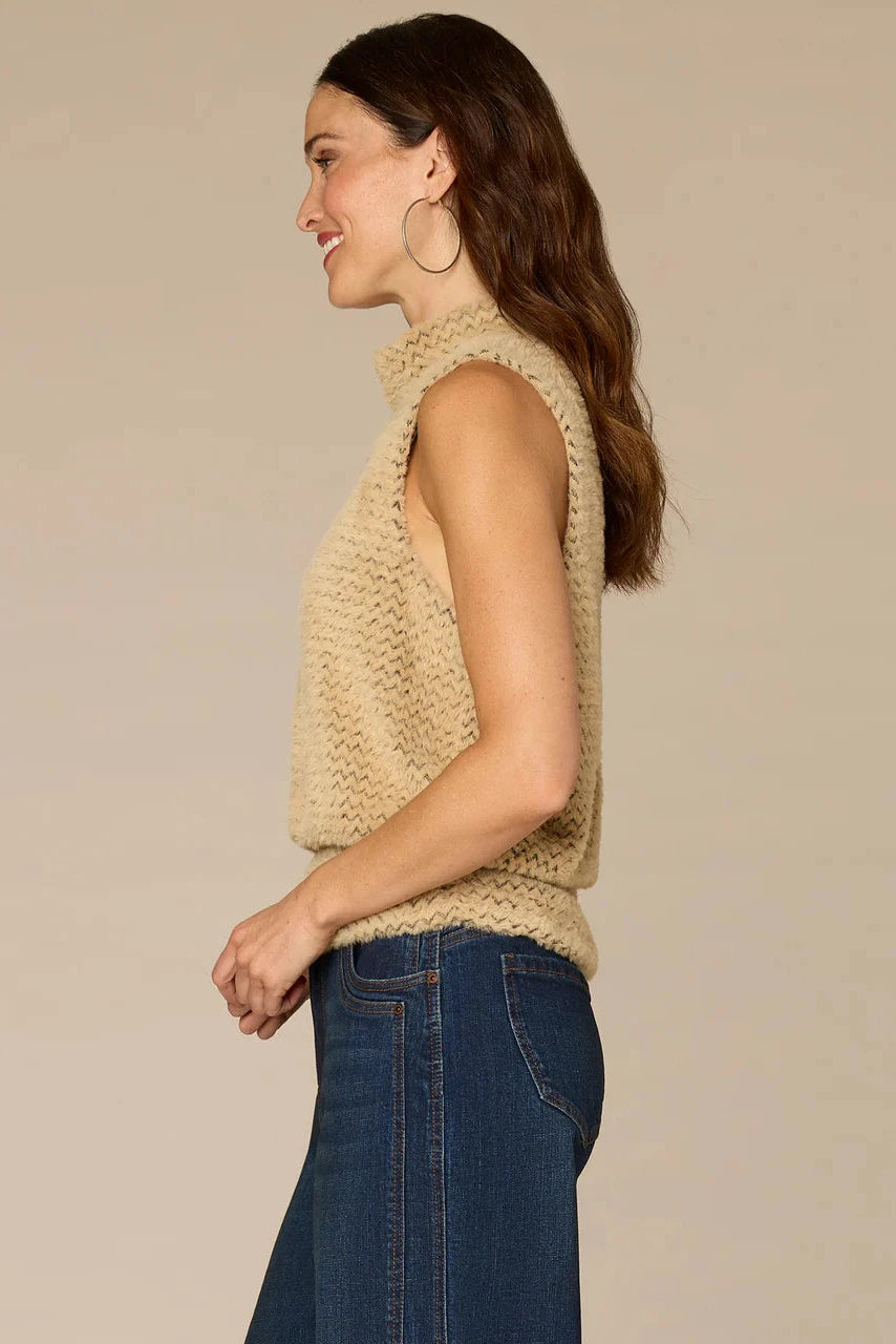 Woman wearing a beige knitted vest and blue jeans against a beige background