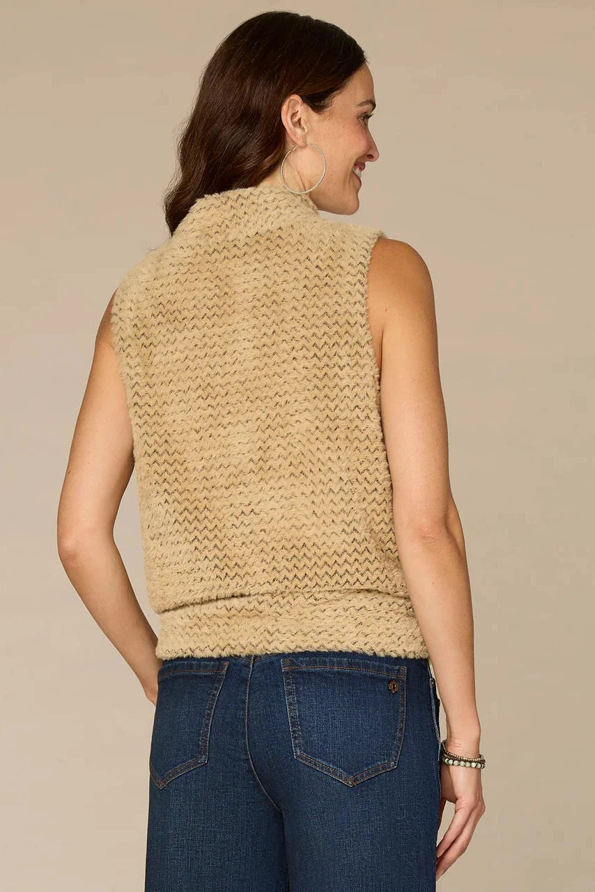 Woman wearing a beige knitted vest and blue jeans on a beige background