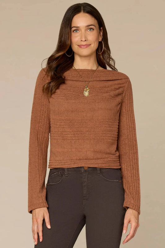 Woman wearing a copper ribbed sweater and dark jeans against a beige background