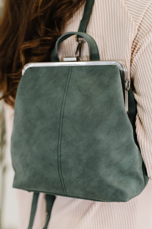 Green leather backpack worn by a person with a blurred background