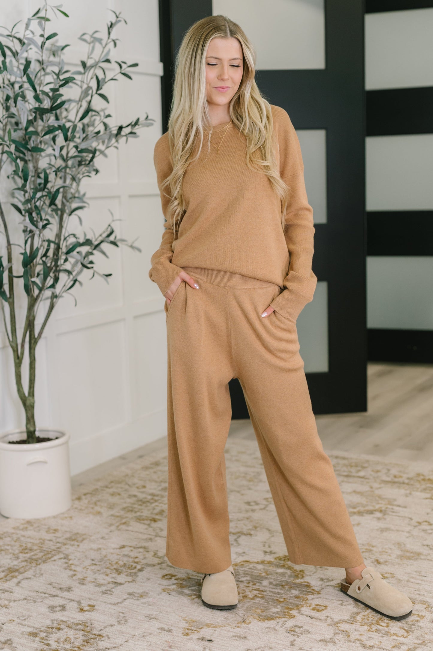 Woman wearing a beige outfit standing in a room with a plant and black and white wall.